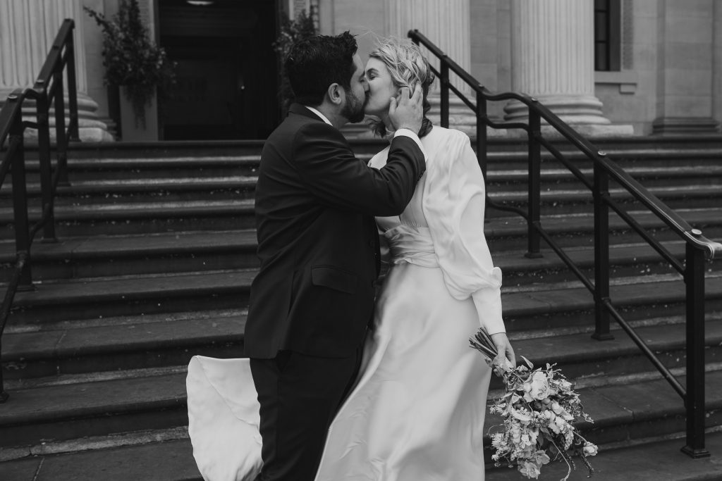 Black and white photo of bride and Groom kissing at the bottom of the steps outside Old Marylebone Town Hall