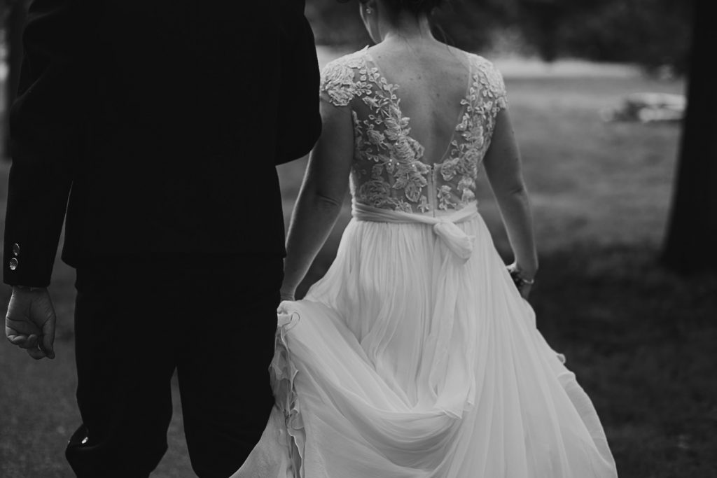Black and white detail shot of bride's dress as she walks with groom through London park