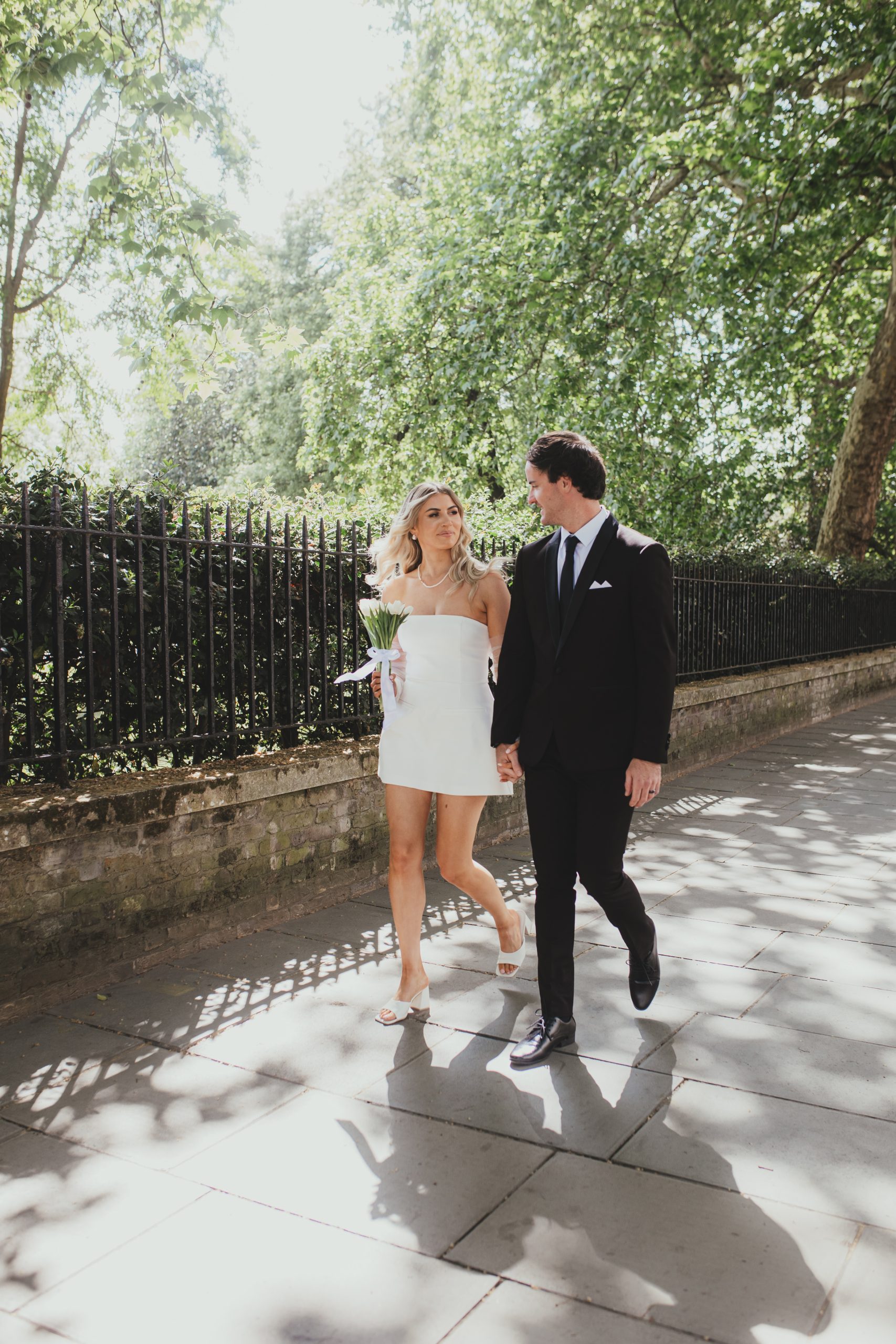 Bride and groom walking hand in hand along a leafy London street