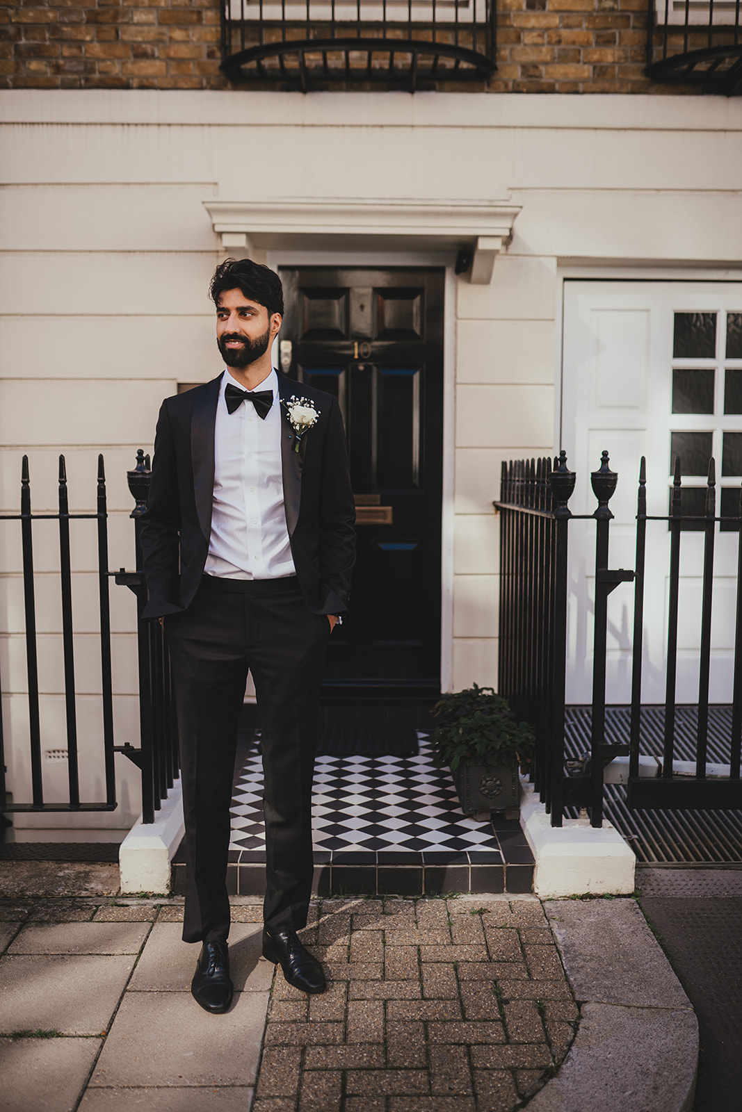 Groom in a tuxedo posing outside a London townhouse doorway.