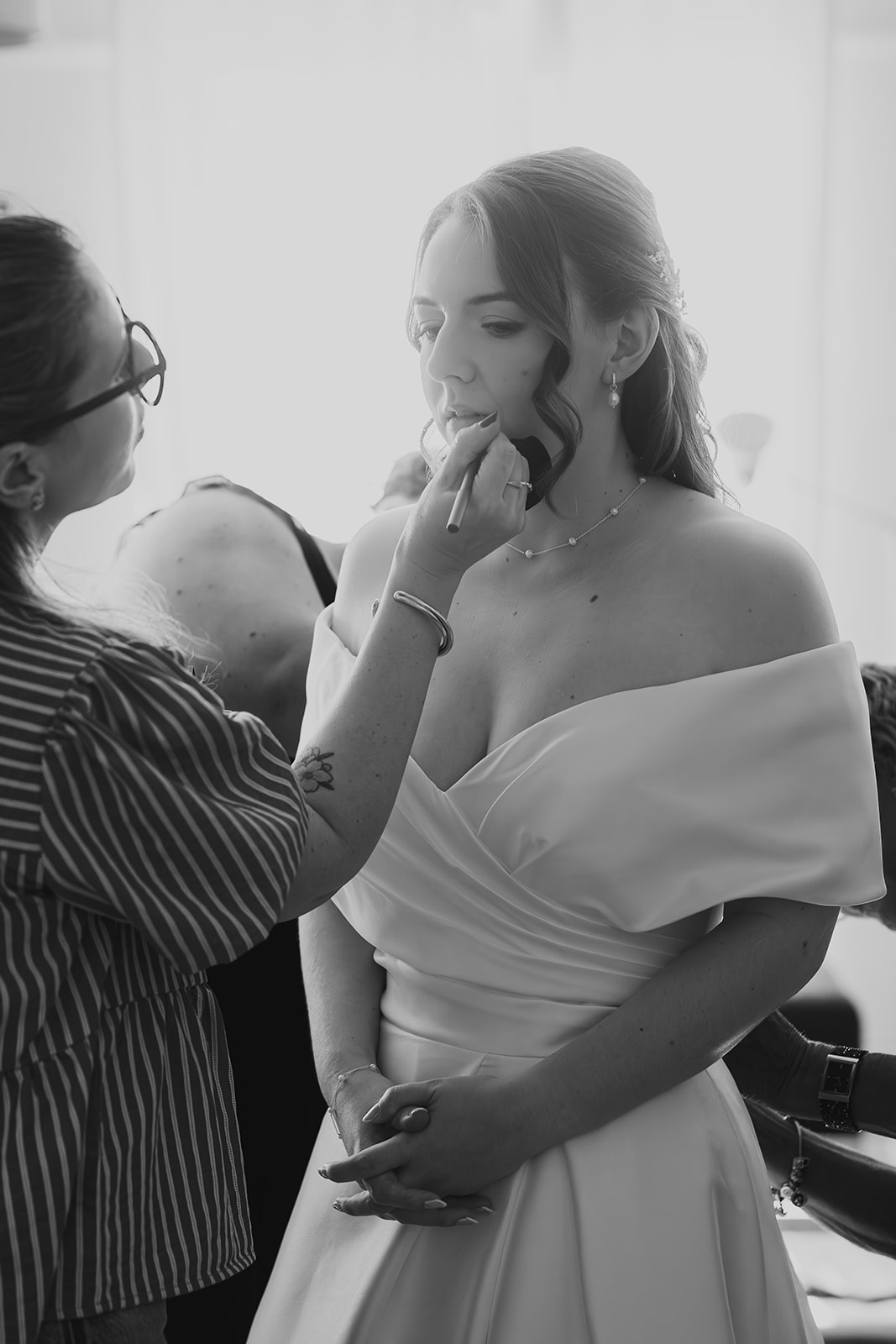 Bride having her makeup touched up in natural window light.
