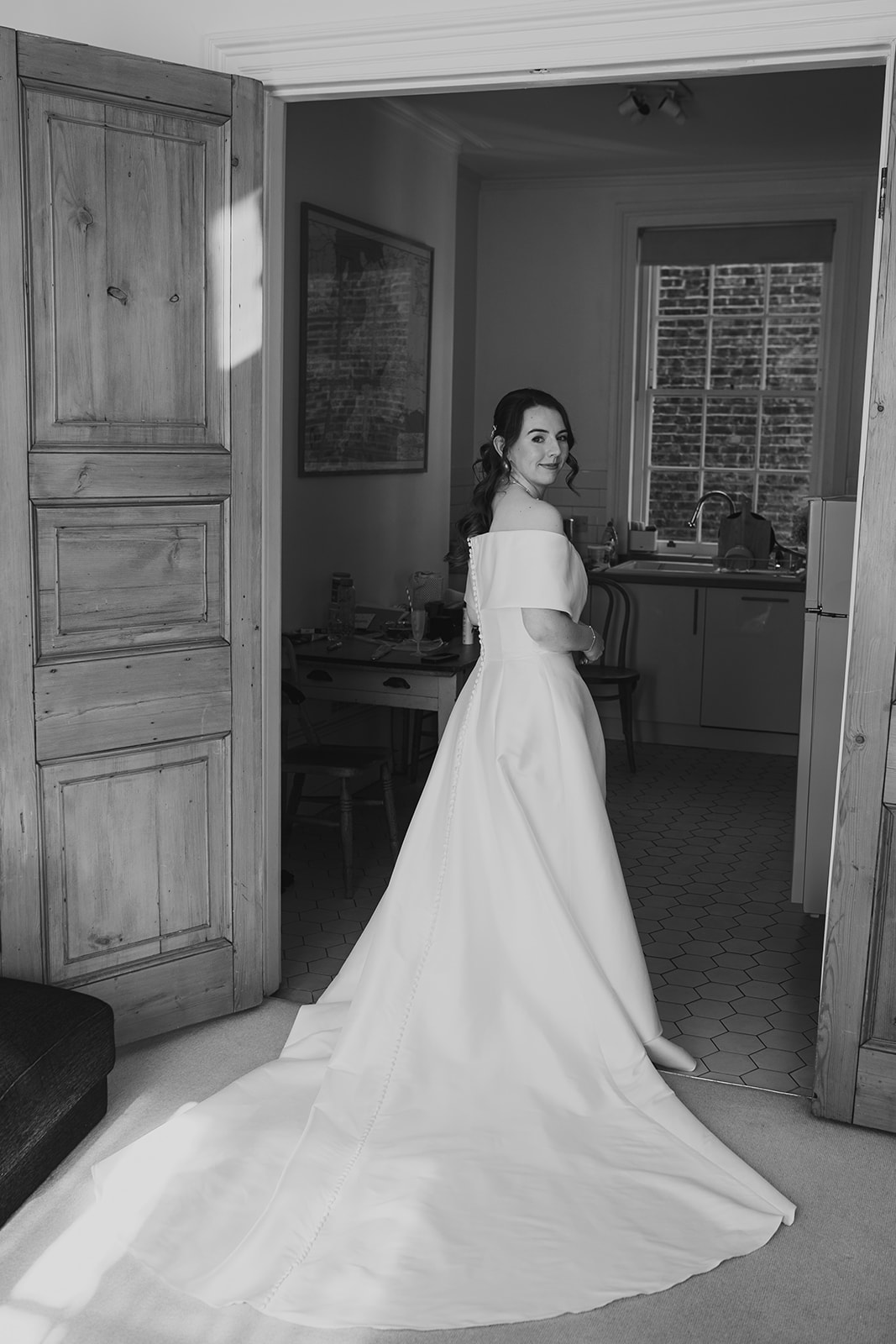 Bride in her wedding dress standing in a doorway, black-and-white portrait.