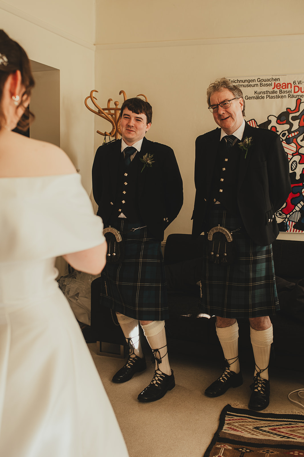 Two men in kilts smiling at the bride during pre-ceremony moments at home.