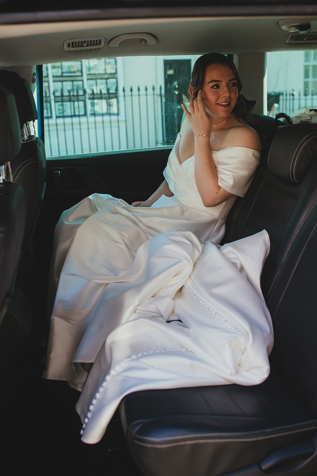 Bride sitting in the back of a black cab in her wedding dress, looking out the window.