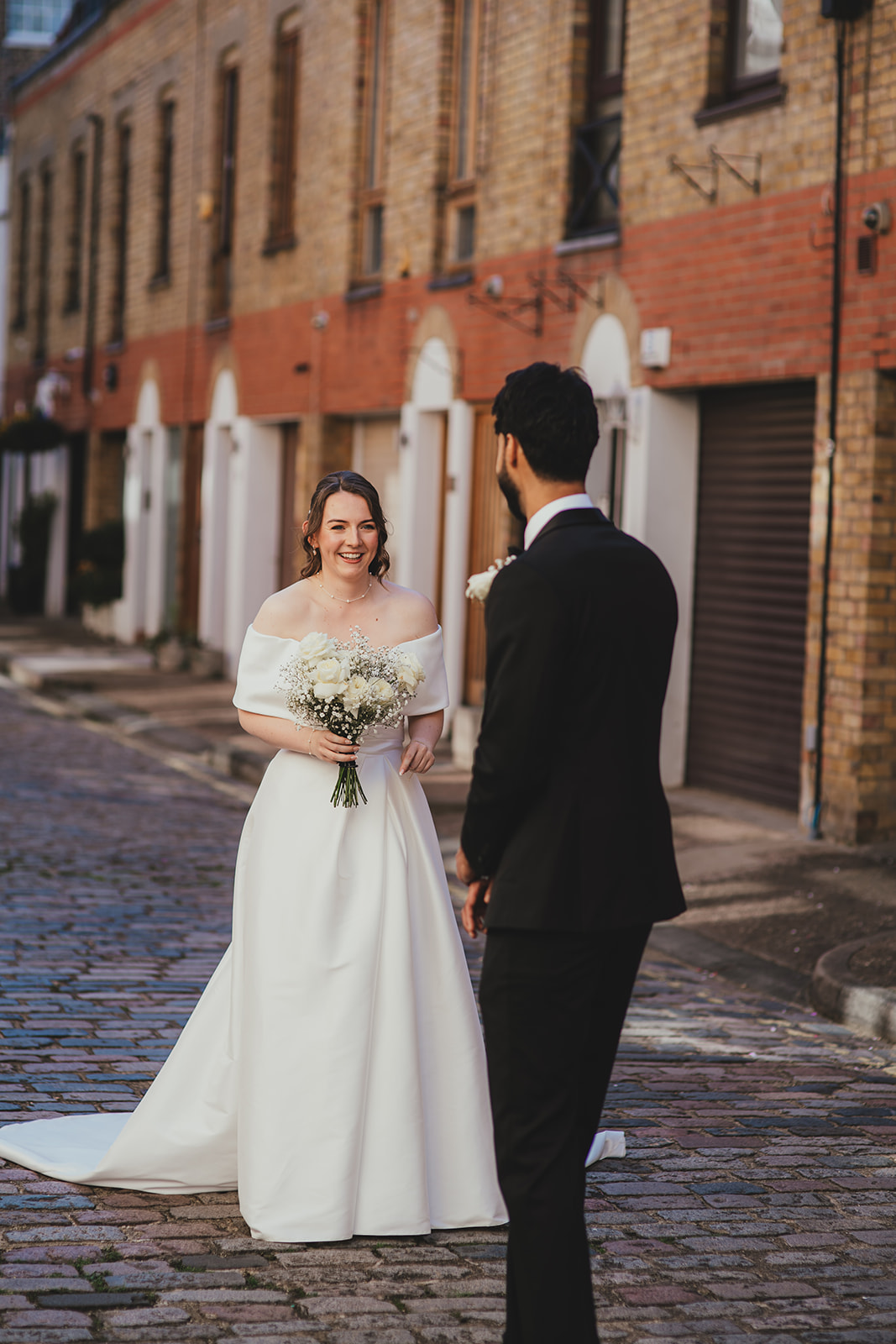 Bride smiling at the groom during their first look on a cobbled London mews