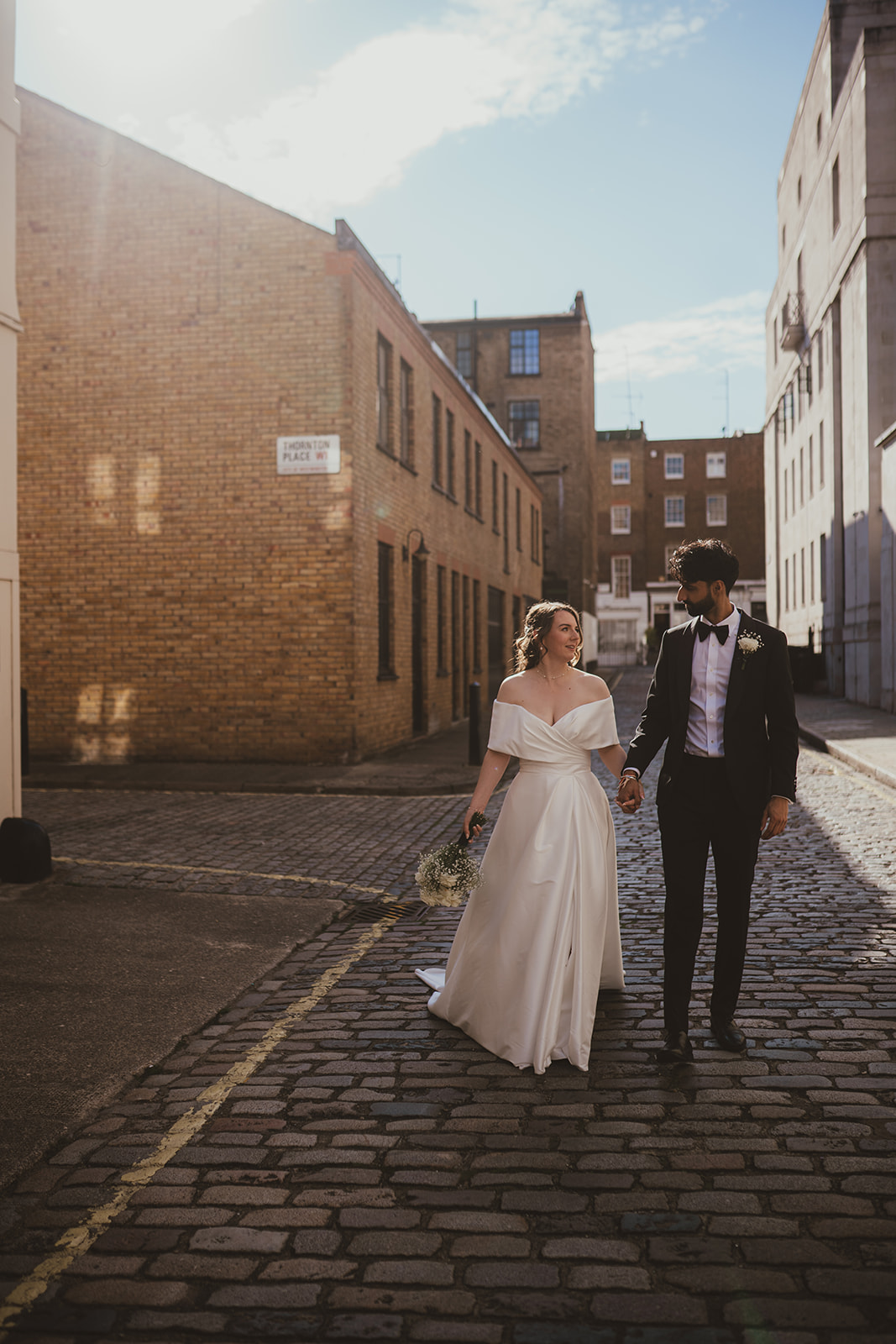 Bride smiling at the groom walking on a cobbled London mews, Old Marylebone Town Hall