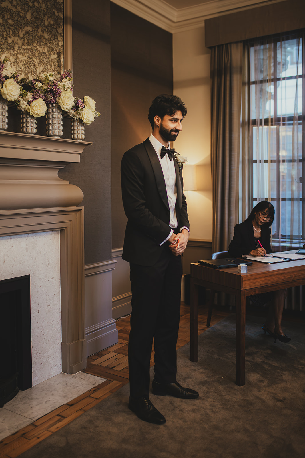 Groom stands at the front of the Mayfair Room at Old Marylebone Town Hall as the registrar prepares paperwork