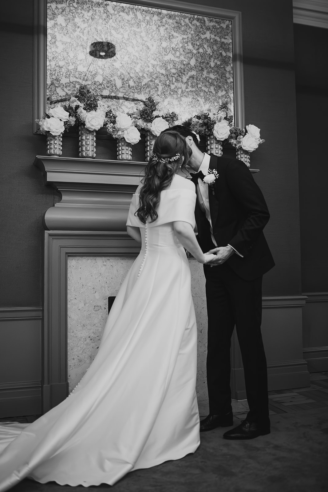 Black and white photo of the couple kissing in front of a flower-decorated mantelpiece at Old Marylebone Town Hall