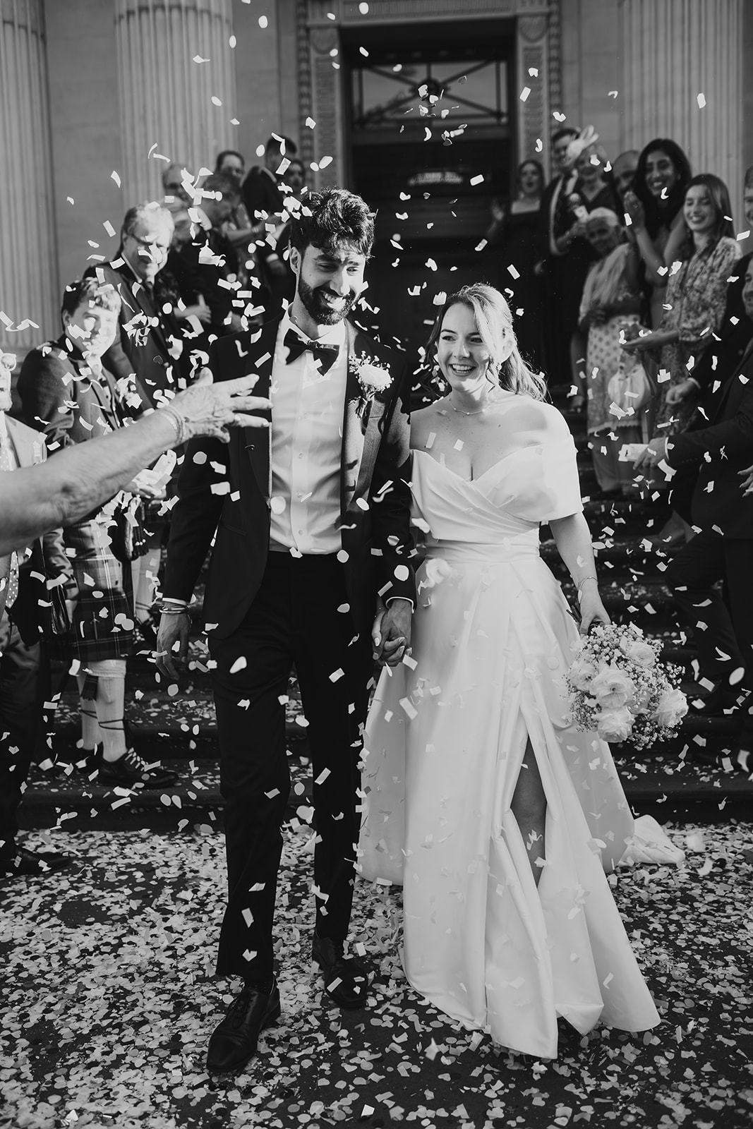 Bride and groom walk out of Old Marylebone Town Hall as confetti falls (black and white)