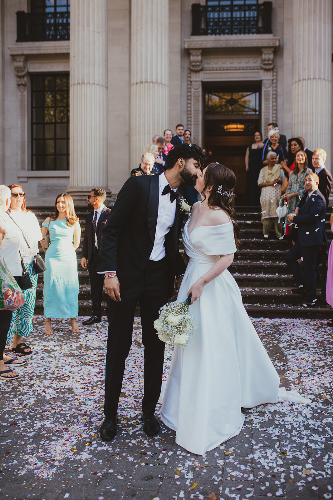 Bride and groom kiss on the steps outside Old Marylebone Town Hall as guests watch