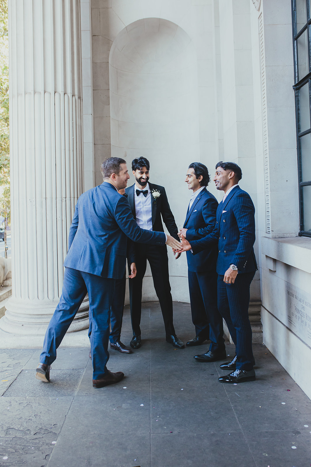 Groom laughs with friends outside Old Marylebone Town Hall colonnade, London