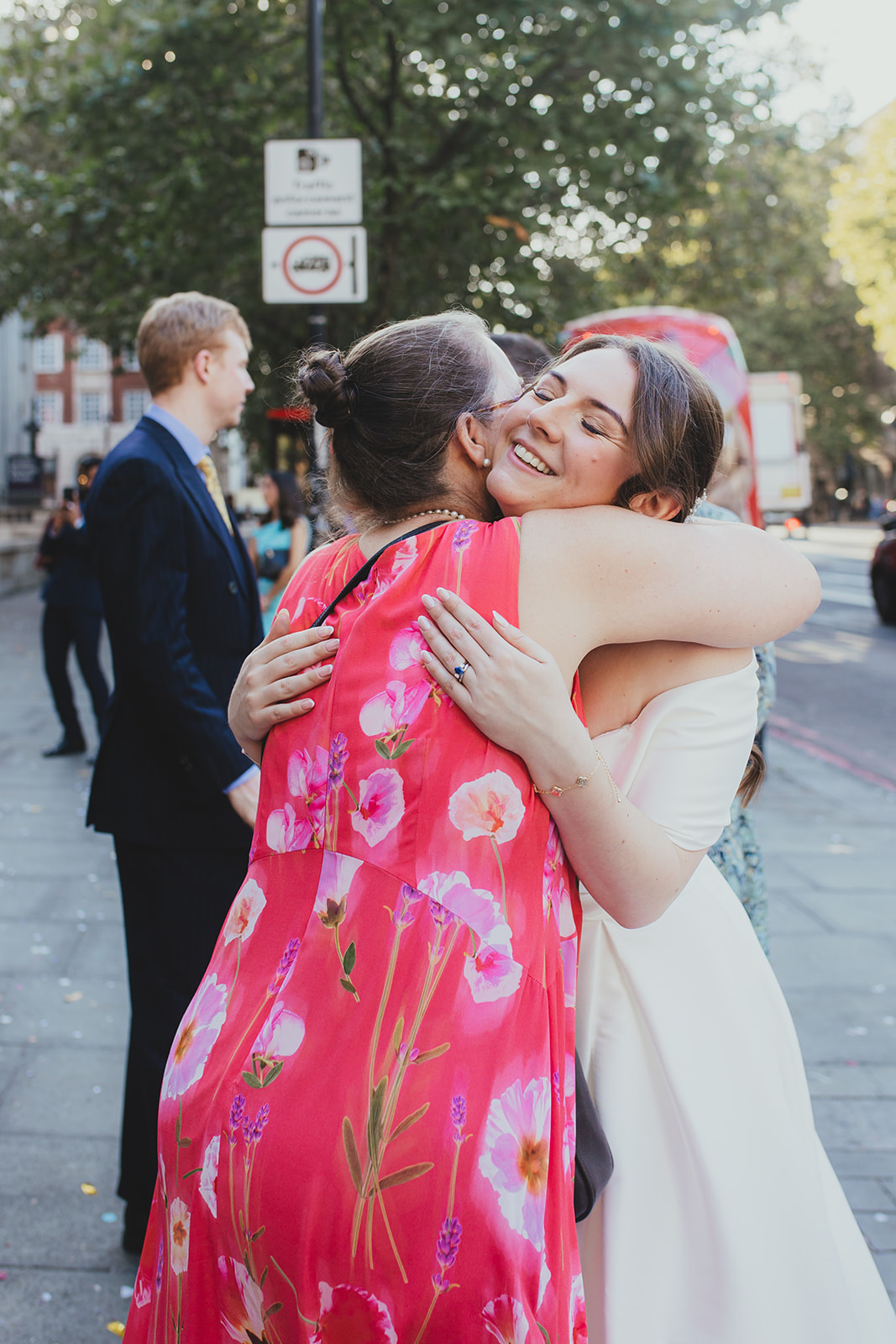 Bride hugs a guest in a bright pink dress outside Old Marylebone Town Hall, London