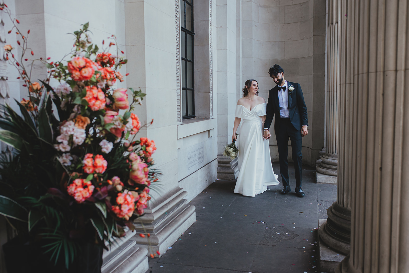 Couple walk past colourful flowers and stone columns outside Old Marylebone Town Hall, London