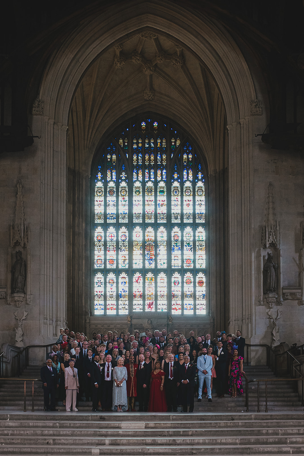 Group photo of wedding party in front of stained glass window inside the Palace of Westminster, London