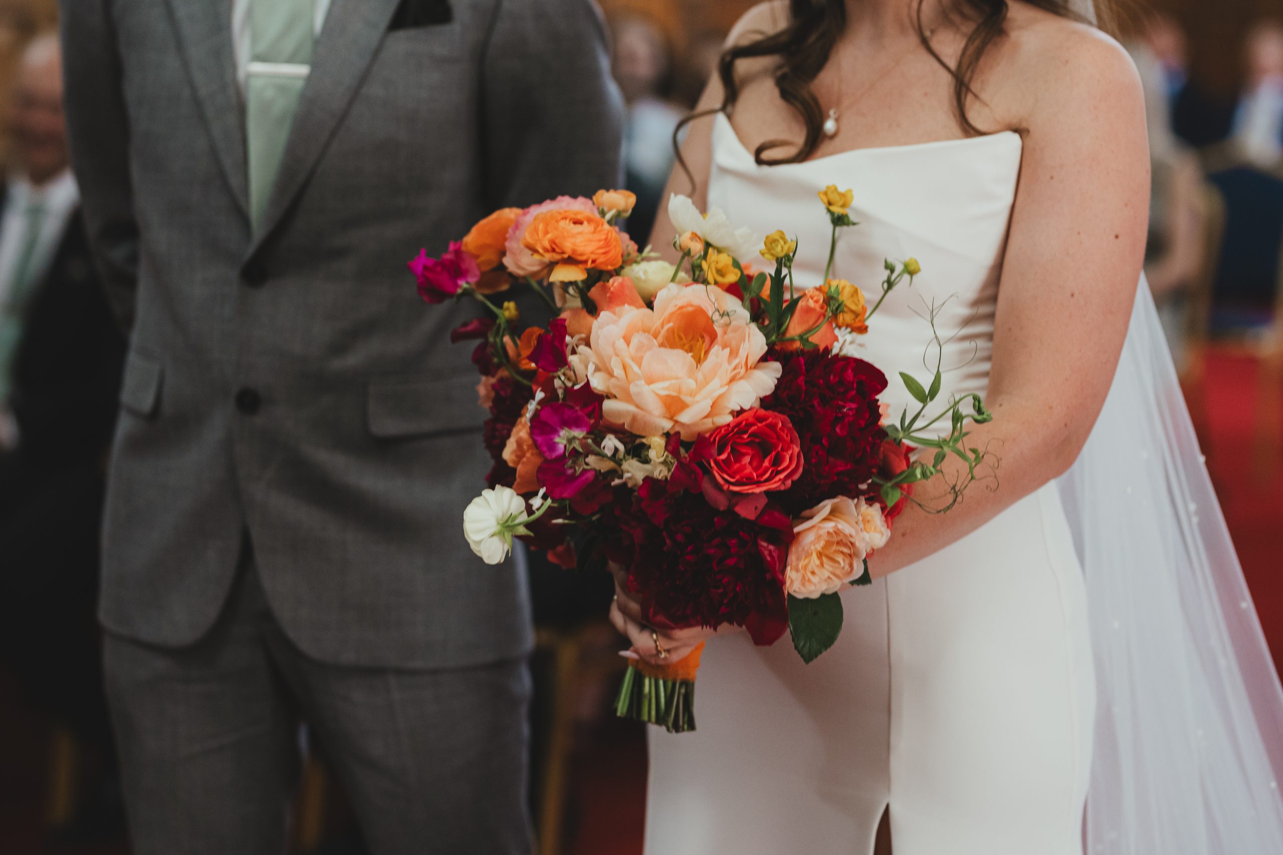 Wedding bouquet of colourful orange, red and peach flowers held by bride during ceremony at Islington Town Hall, London wedding
