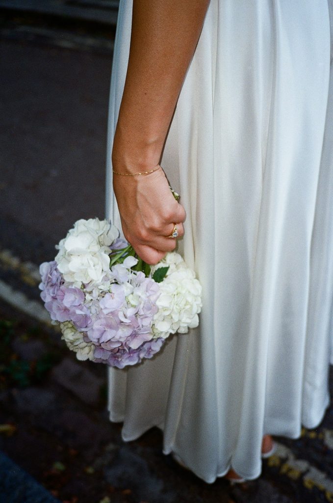 A detail photo of the bride's hydrangea bouquet whilst she holds it downwards at her side