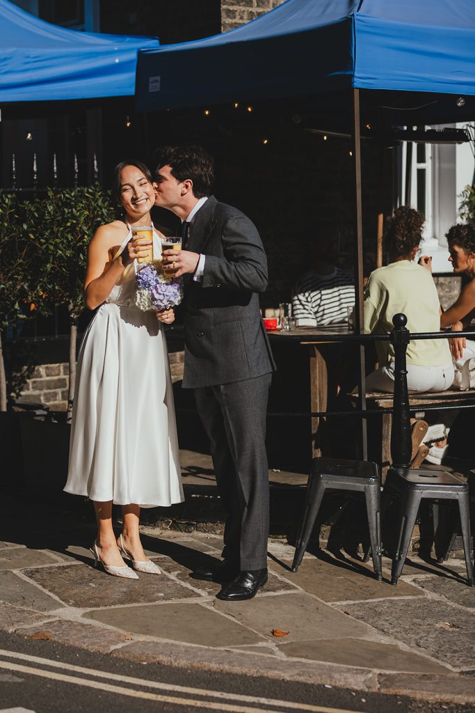 Groom kisses bride on cheek outside the pub