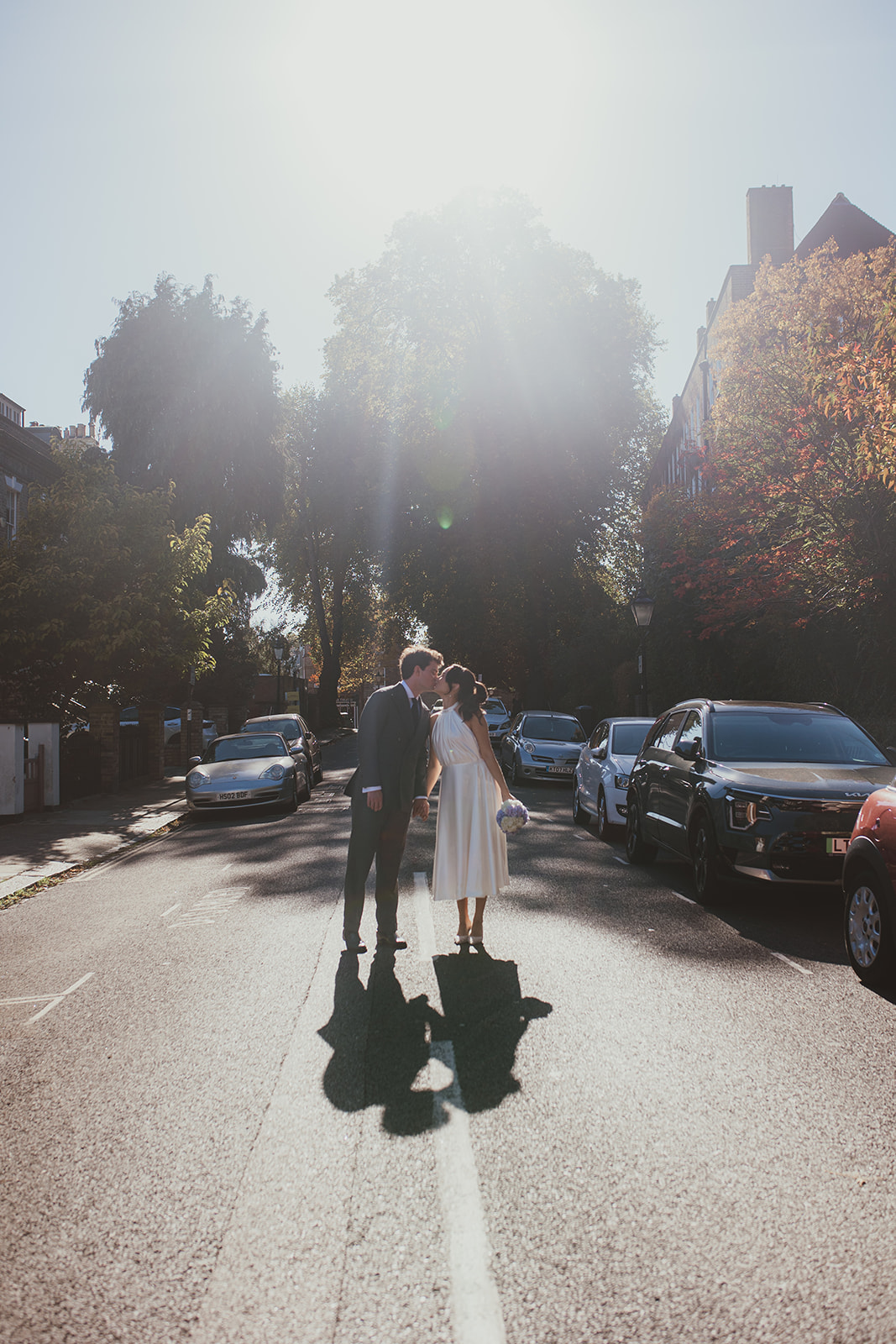Bride and groom kissing in the middle of the road with the soft sunshie behind them