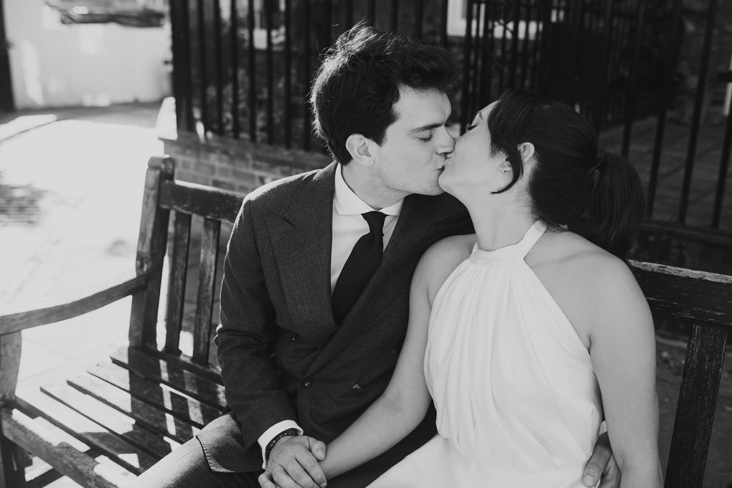 Black and whit of bride and groom kissing on a bench
