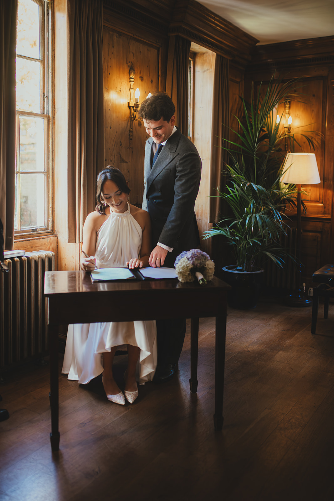 Bride signing the marriage certificate with groom standing next to her