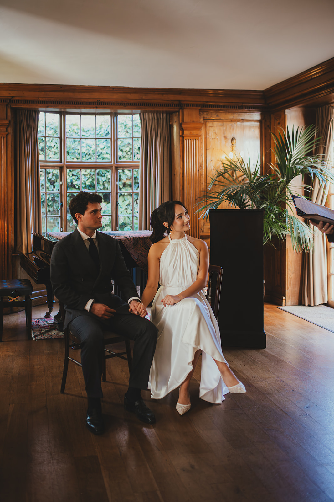 Bride and groom sitting next to each other during their wedding ceremony inside the music room at Burgh House
